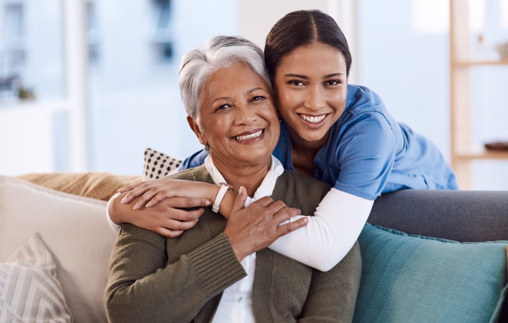 Two women smile as they embrace on a couch, showing warmth and family bond.