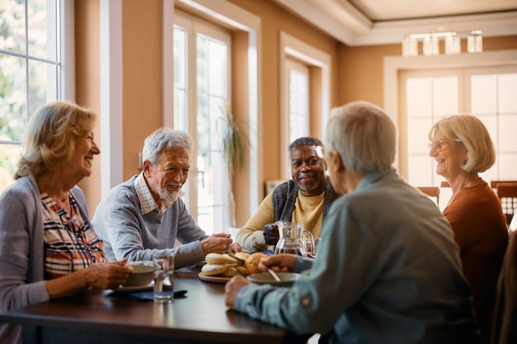 A group of smiling seniors sitting around a table indoors in a personal care community.