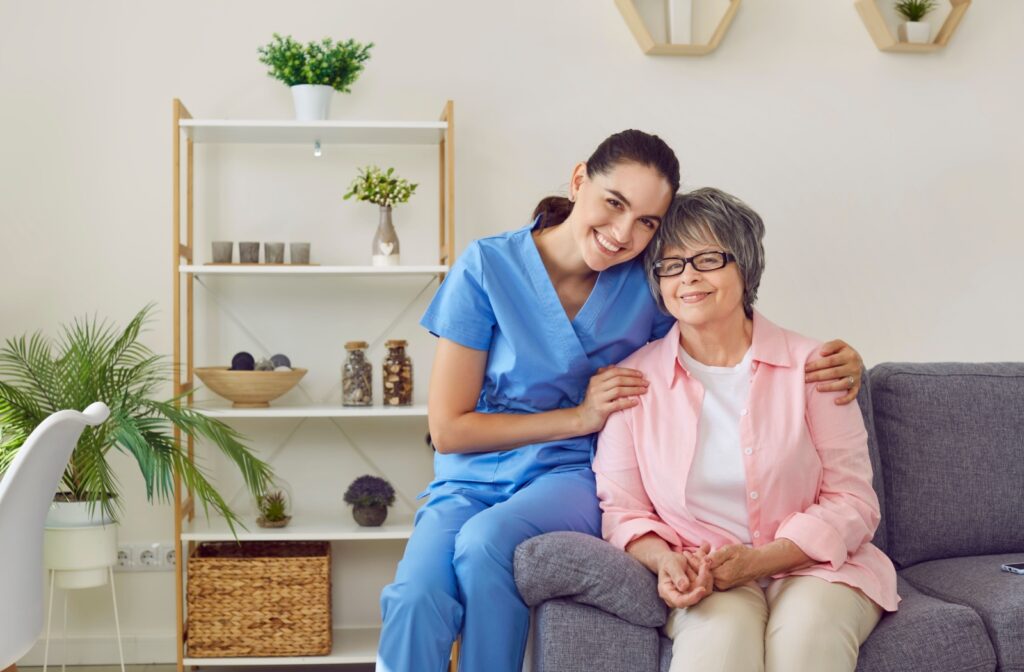 A memory care staff member and a resident sit together on the couch, posing for the camera.