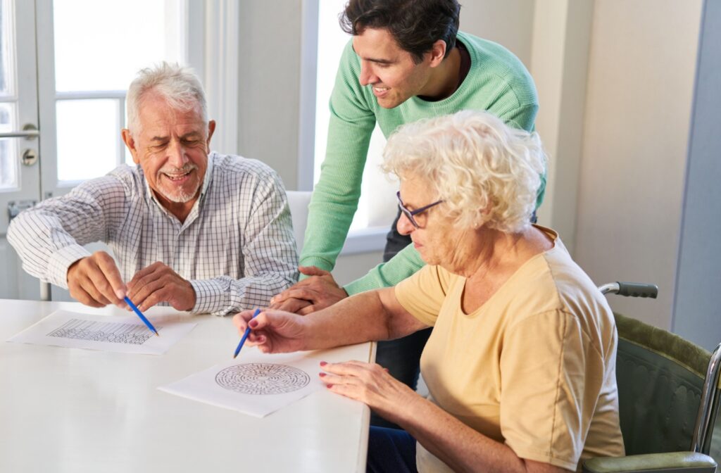 An older couple sitting at a table doing memory puzzles with their adult child watching.