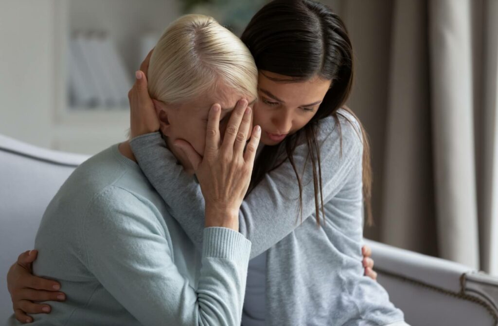 A concerned adult child holds their upset older parent close to try and comfort them