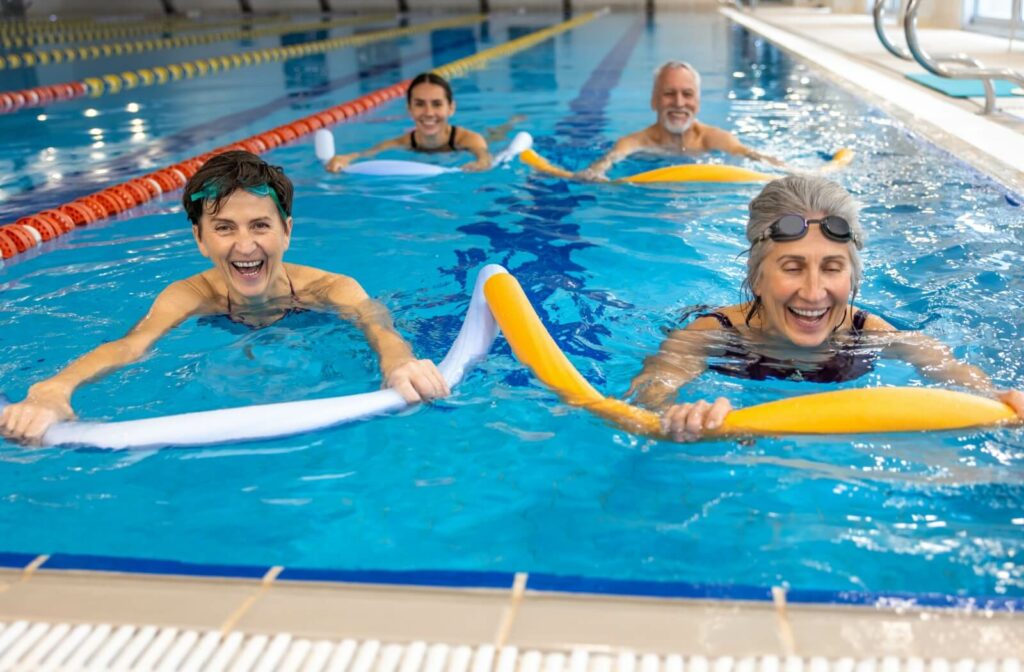 Four seniors use pool noodles as swimming aids as they swim laps in a mostly empty Olympic-sized indoor pool