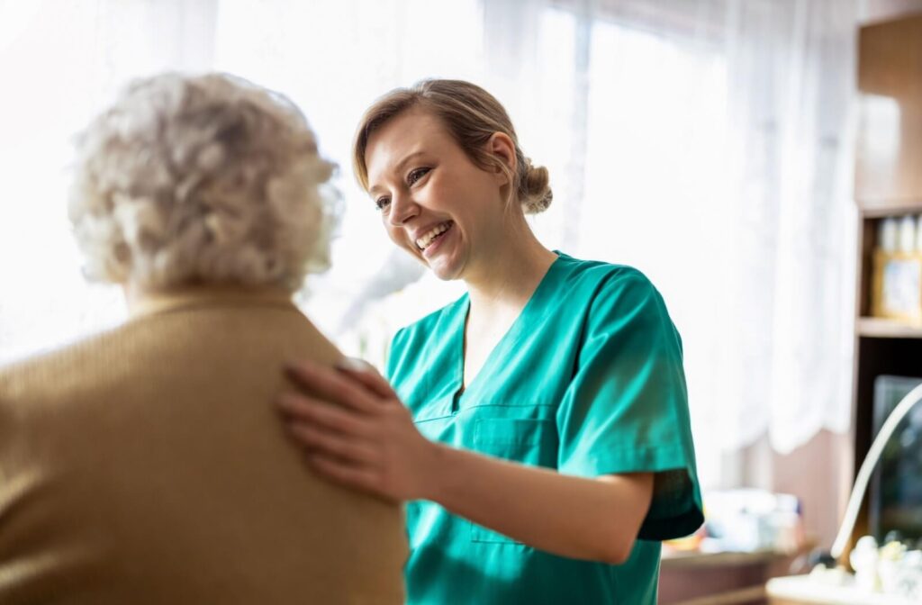 A caregiver touches a resident's back and smiles at them during a checkin in senior living
