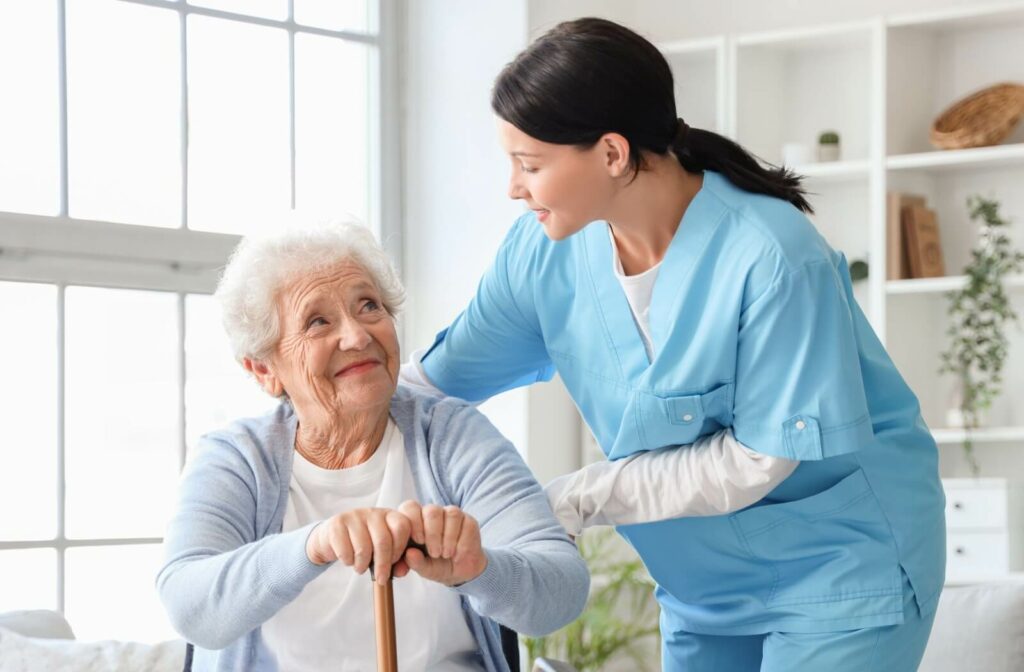 A caregiver helps a senior with a cane stand up in memory care.