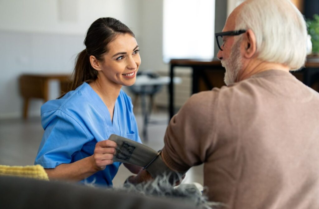 A caregiver in personal care smiles at a resident while wrapping their arm with a blood pressure strap as part of a proactive wellness routine