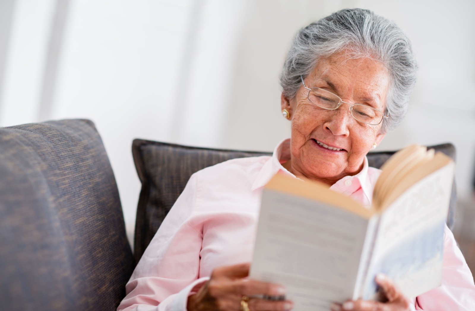 A senior smiles as they enjoy reading a book.
