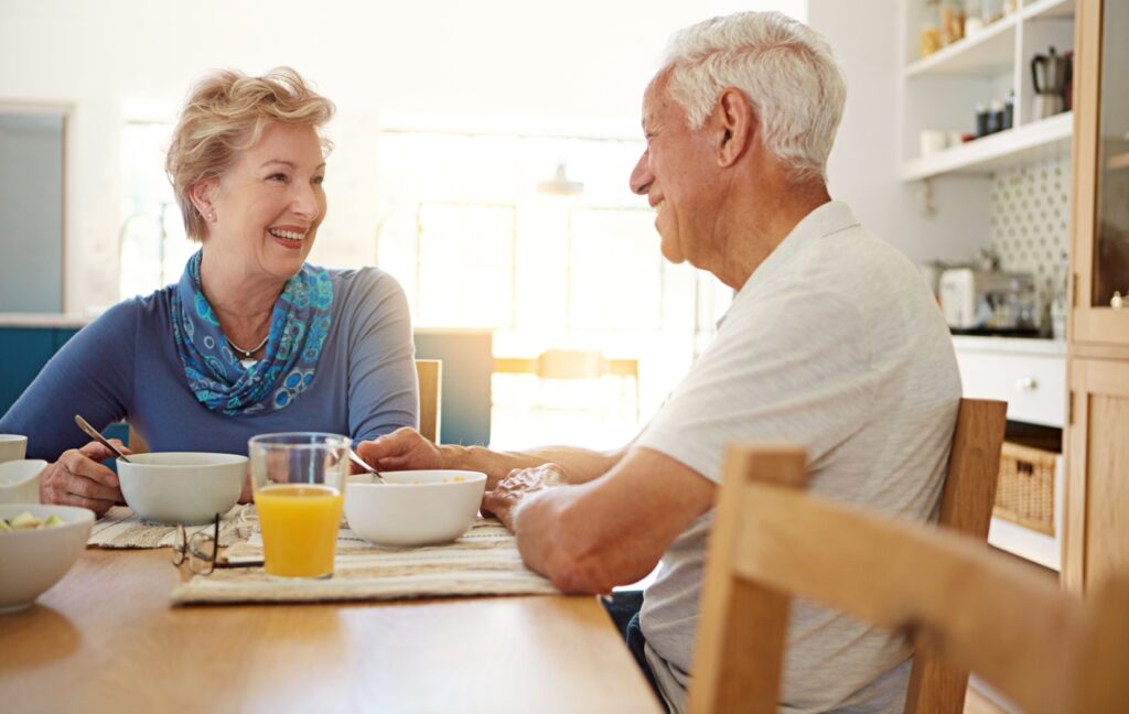 Two senior friends sit at a table in a personal care community, and share breakfast together