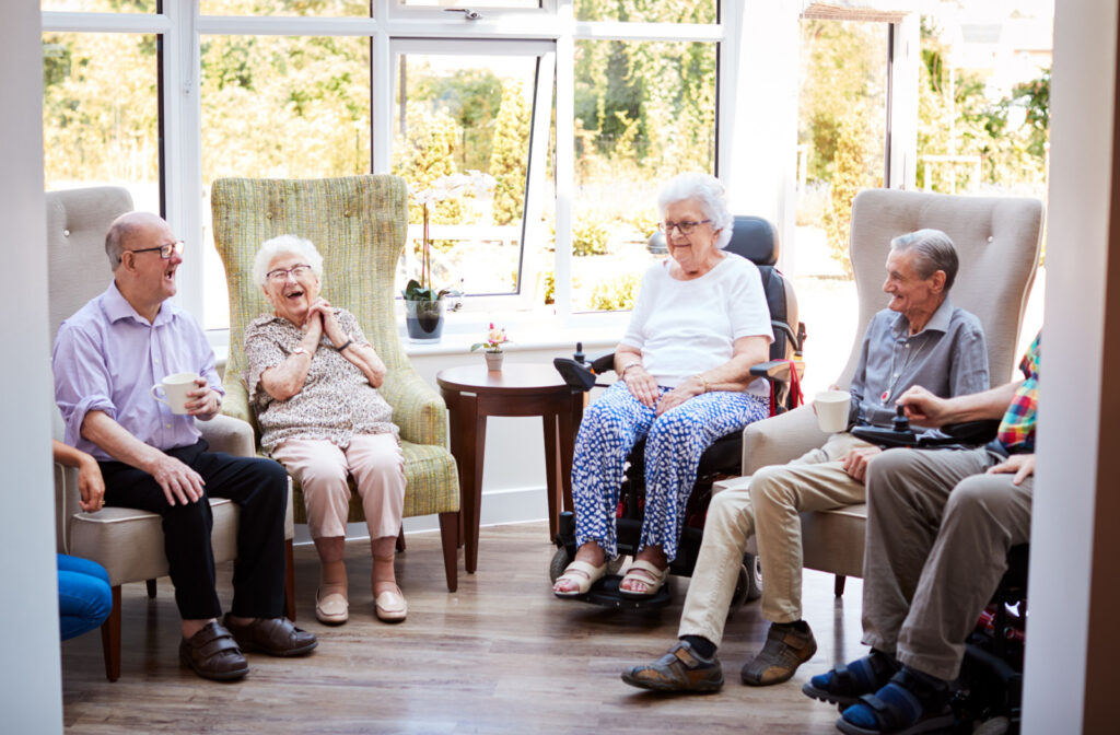 A group of personal care community residents sit in armchairs in a bright room and reminisce together